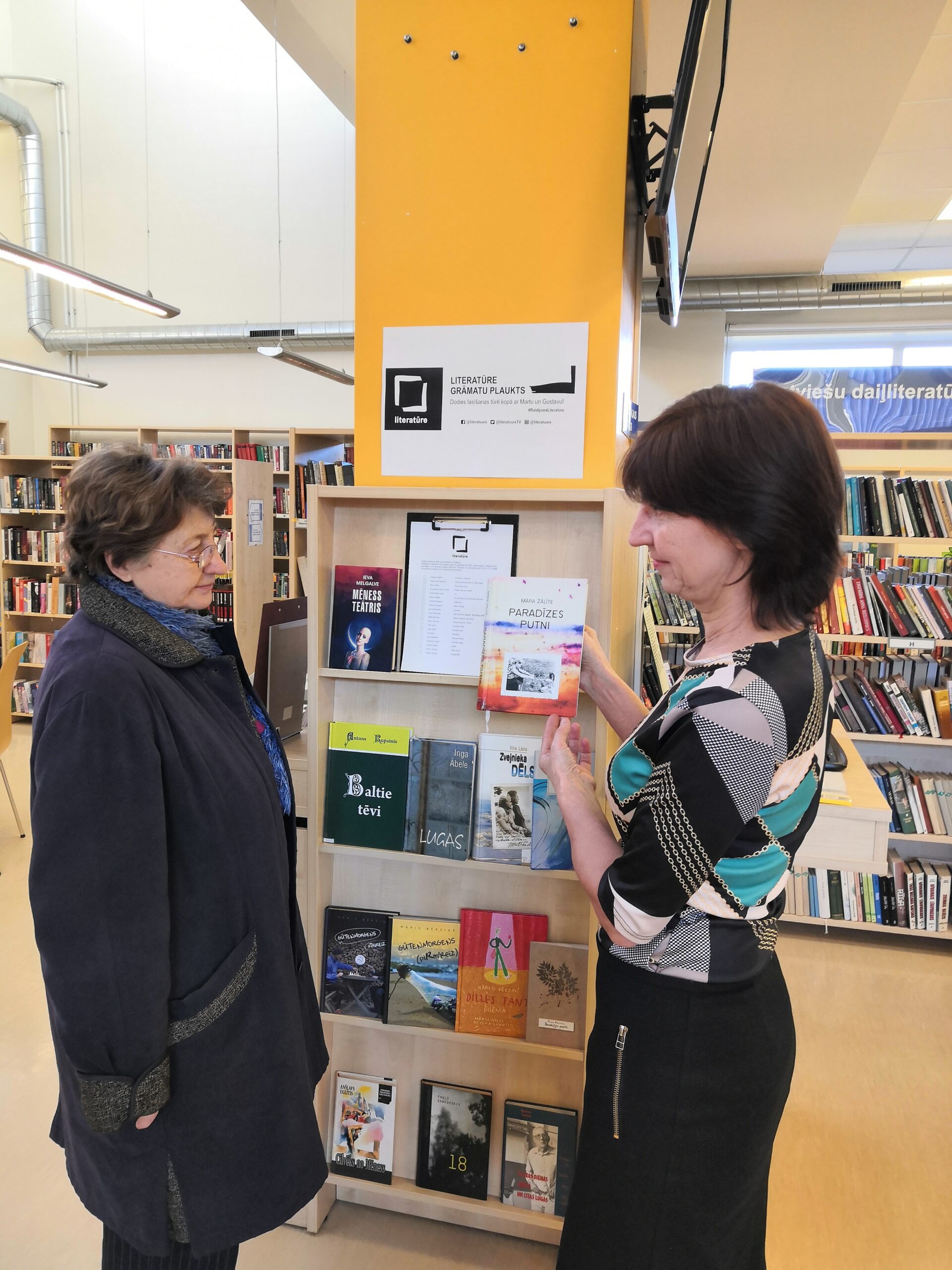 Bibliotekāre Anita Tarvida (no labās) sarunā ar lasītāju pie Literatūres grāmatu plaukta
